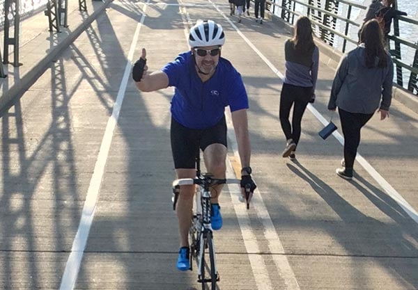 Rob Roe giving a thumbs up while riding on the Stone Arch Bridge